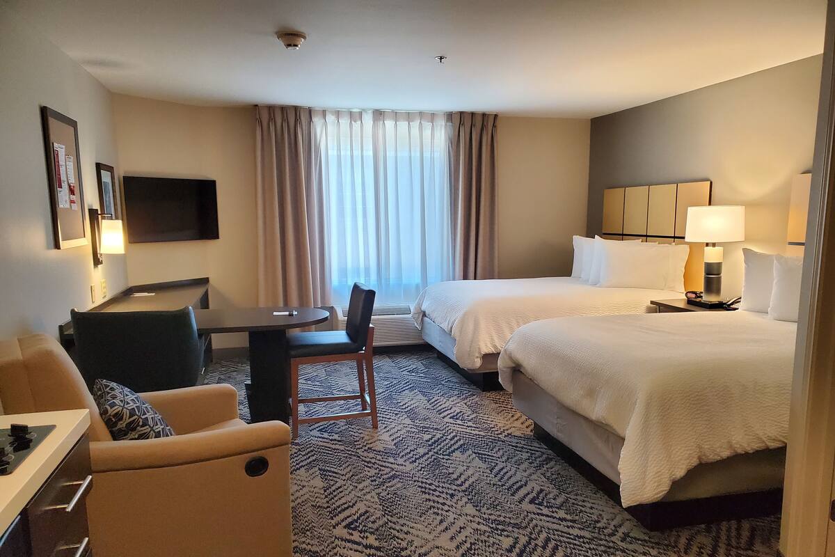 A hotel room with a bed, a desk, a chair, a sofa, and a TV.