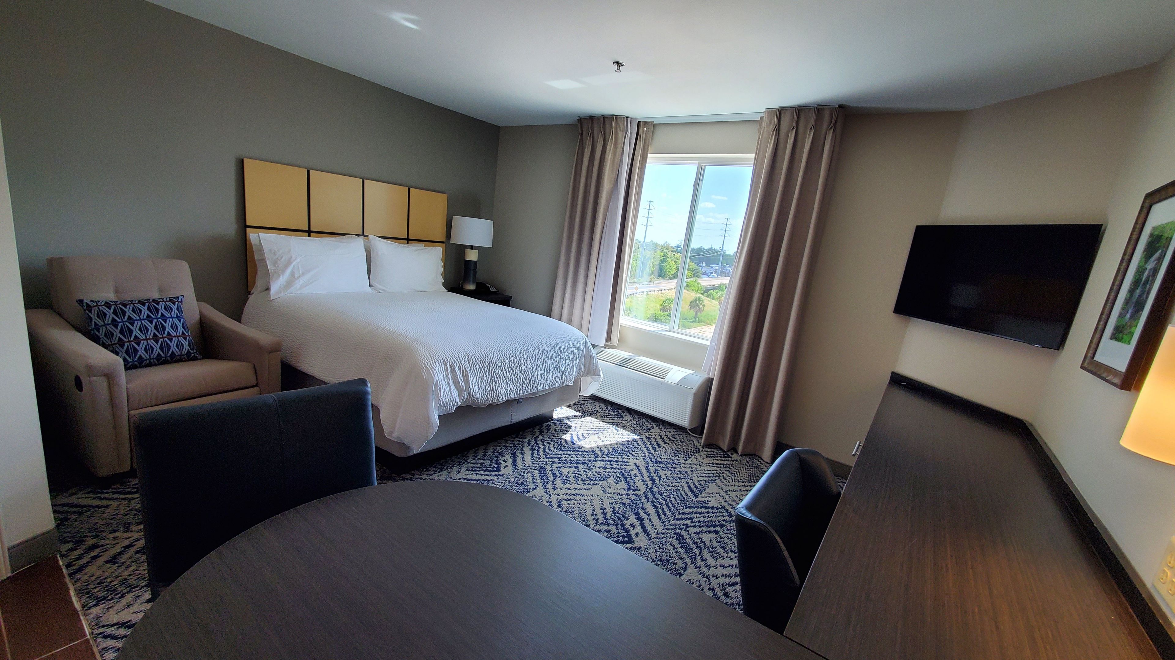 Habitaci ón de hotel con cama, escritorio, silla, televisor y ventana con cortinas.