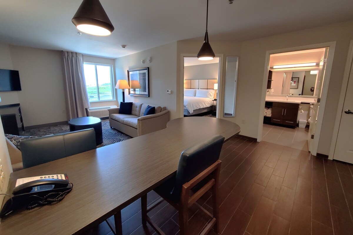 A hotel room with a bed, a desk, a chair, a TV, and a bathroom visible through an open door.