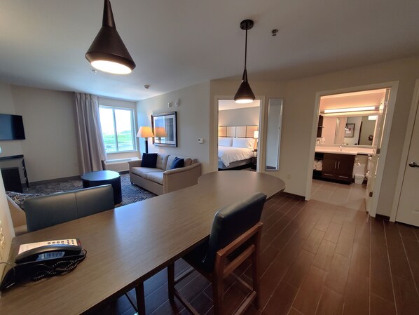 A hotel room with a dining area, a sofa, a TV, a lamp, and a bed.