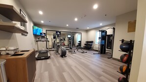 Un gimnasio con máquinas de cardio, pesas libres y un espejo.