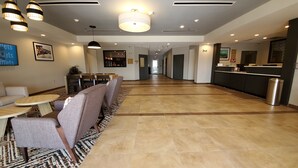 Un vestíbulo de hotel con un mostrador de recepción alargado, una zona de estar con sofás y mesas, y una alfombra estampada.