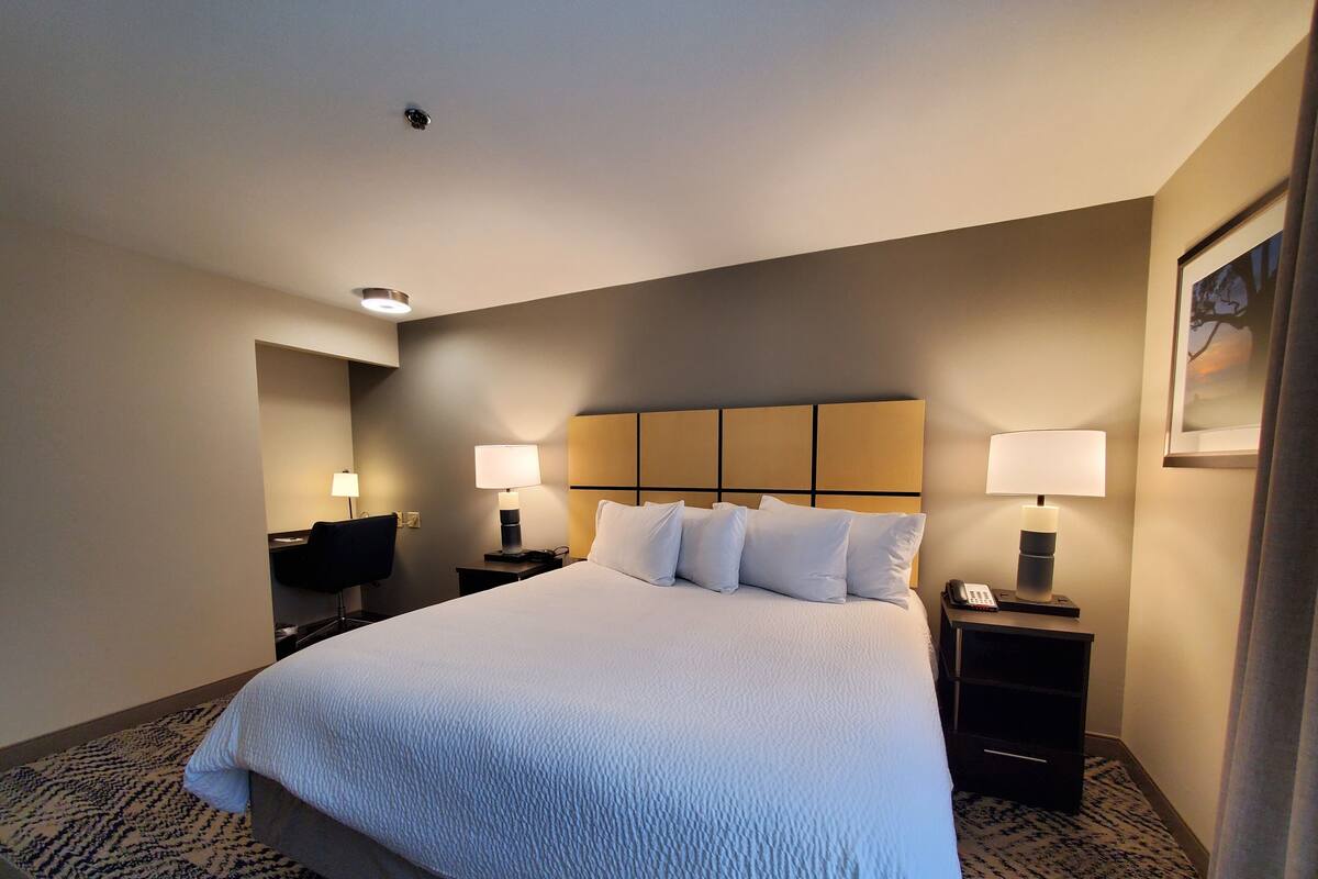 A hotel room with a large bed, two bedside tables with lamps, a desk with a chair, and a framed picture on the wall.