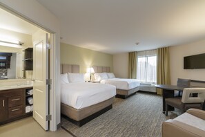 Habitación de hotel con dos camas, un escritorio, una silla, un televisor y un baño con espejo y lavamanos.