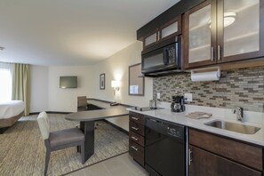 Quarto de hotel moderno com cozinha compacta, televisão de tela plana, área de refeições e uma cama.
