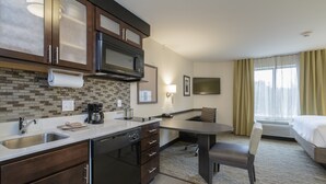 A hotel room with a kitchenette, a dining area, and a bed.