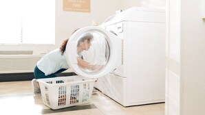 A person loading a white laundry basket into a front-loading washing machine in a well-lit room with a sign indicating free washer and dryer use. - Candlewood Suites Mishawaka North by IHG (Mishawaka)