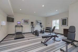 Sala de ginástica com esteira, elíptico, bicicleta ergométrica e banco de musculação.