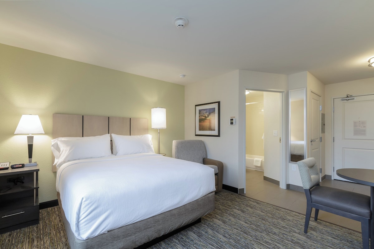 Una habitación de hotel con cama, lámparas de noche, una silla, escritorio y puerta que da a un baño.