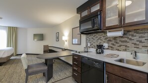 A compact hotel room with a kitchenette, a dining area, a bed, and a TV.