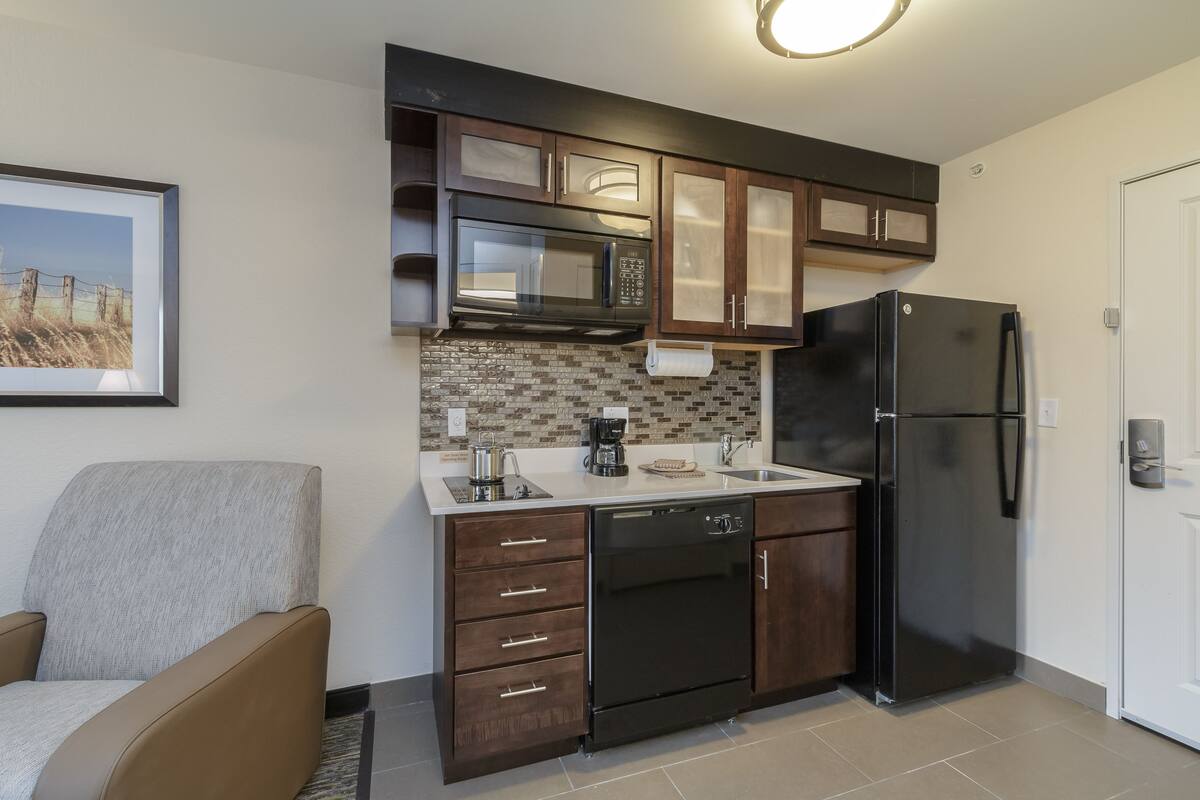 A modern kitchen with dark wooden cabinets, a black refrigerator, a microwave, and a dishwasher.