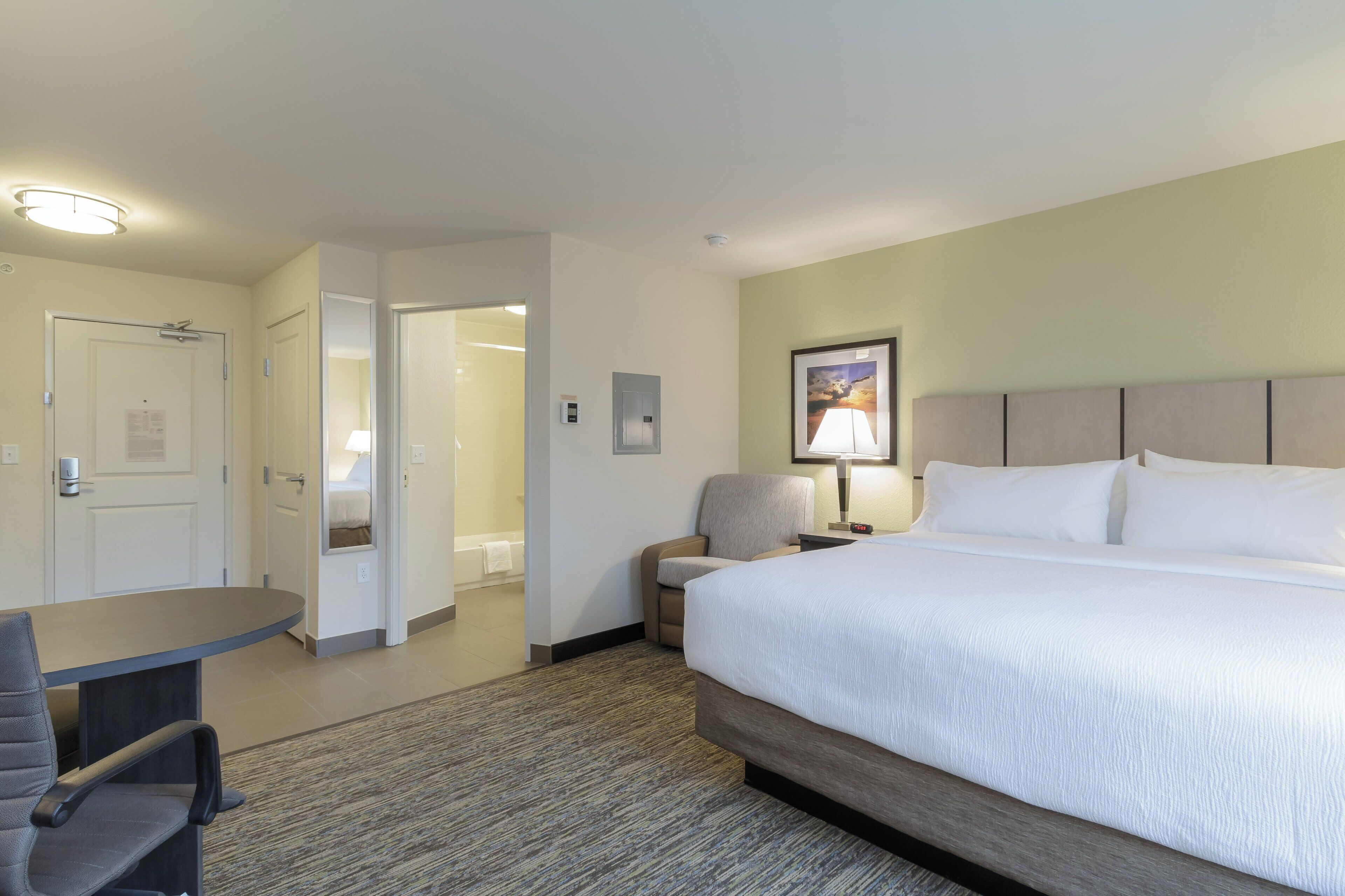Una habitación de hotel con cama, escritorio, silla, lámpara y puerta.