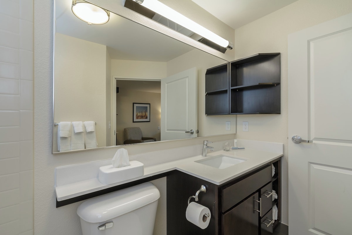 Un baño moderno con un lavamanos blanco, un inodoro, un espejo y un mueble de tocador de color oscuro.