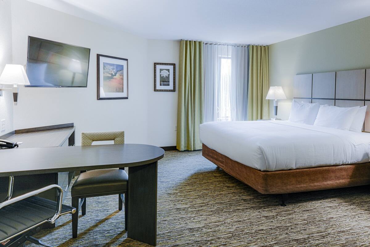 Quarto de hotel com cama, mesas de cabeceira, escrivaninha e cadeiras.