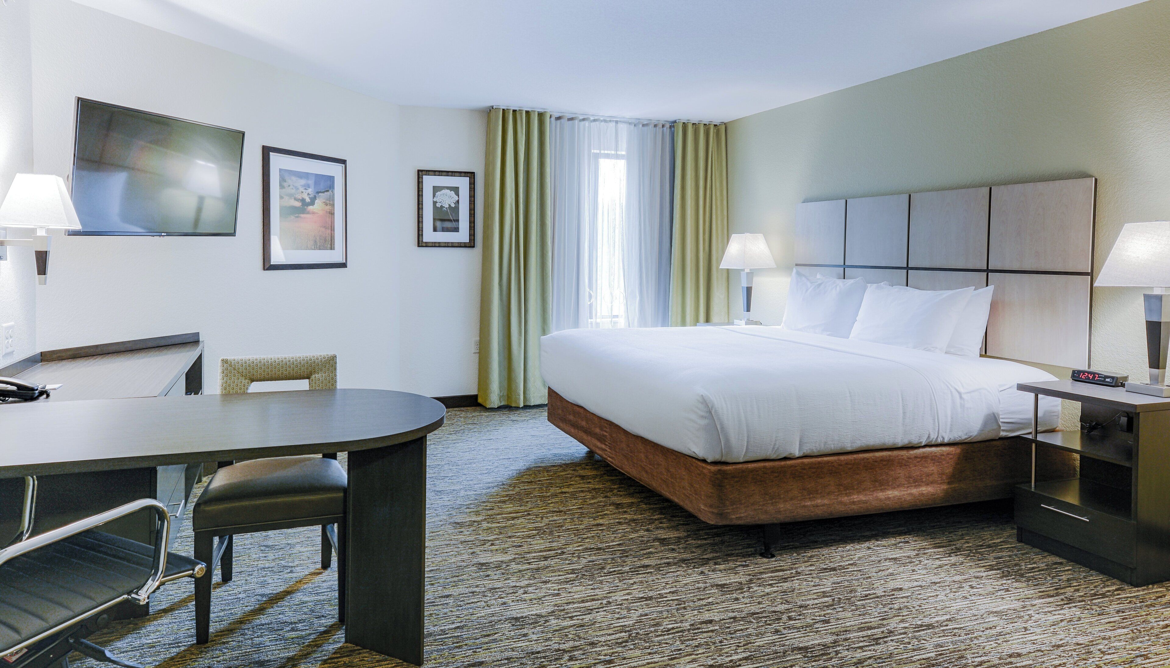 A hotel room with a bed, a desk, a chair, a TV, and a window with curtains.
