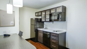 A modern kitchen with stainless steel appliances, dark cabinetry, and a wooden dining table. - Candlewood Suites Lakeville I-35 by IHG (Lakeville)