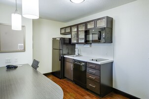 Una cocina moderna con electrodomésticos de acero inoxidable, armarios oscuros y una mesa de comedor de madera.