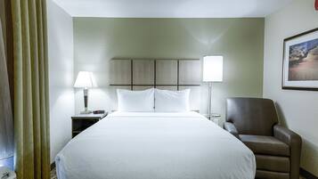 A hotel room with a large bed, two bedside lamps, a chair, and a headboard with a built-in shelf.