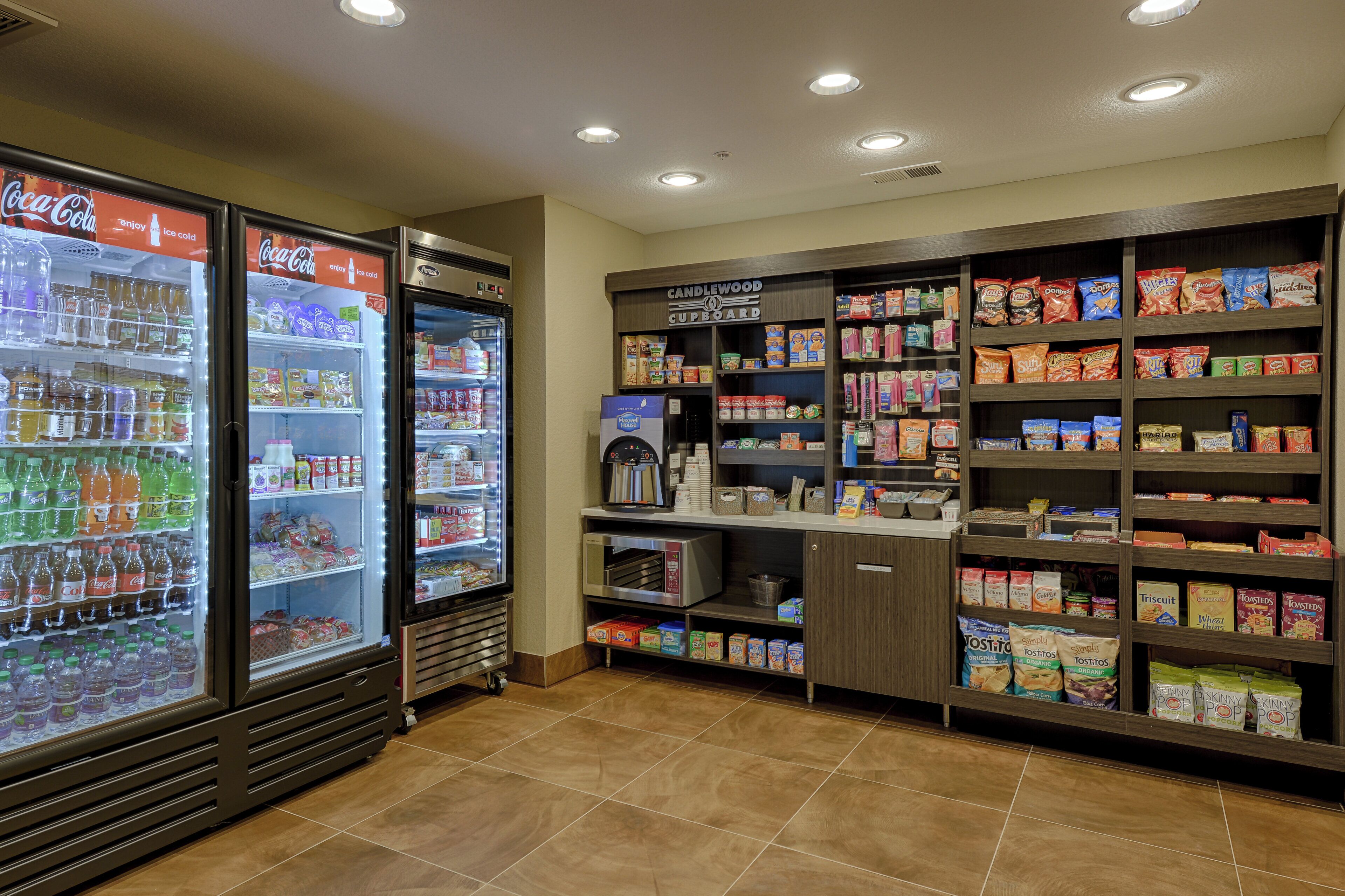 Espaço de autosserviço com máquinas de bebidas refrigeradas, café e prateleiras com lanches e acompanhamentos.