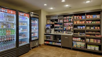 Espaço de autosserviço com máquinas de bebidas refrigeradas, café e prateleiras com lanches e acompanhamentos.