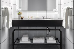 Un baño moderno con encimera negra, baldosas blancas, un lavamanos y varias toallas.
