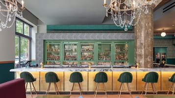 A bar area with a marble countertop, green bar stools, and a decorative chandelier.