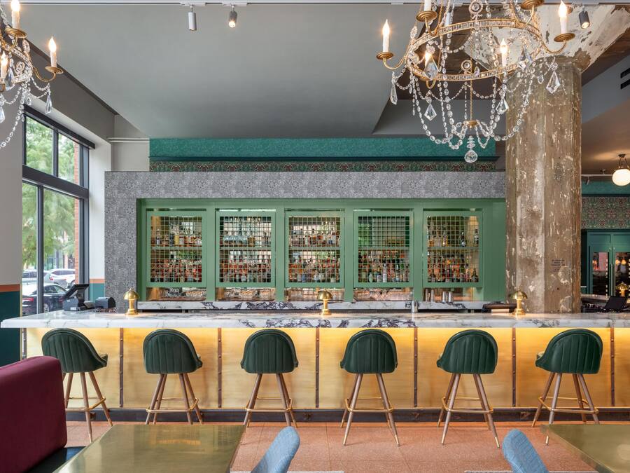 A bar area with a marble countertop, green bar stools, and a decorative chandelier.