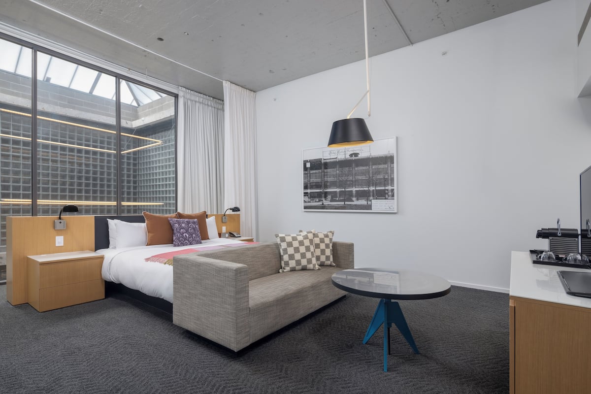 Una habitación de hotel moderna con una cama, un sofá, una mesita y una zona de escritorio.