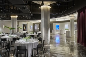 A spacious, well-lit banquet hall with round tables set for dining, large pillars, and a polished floor.