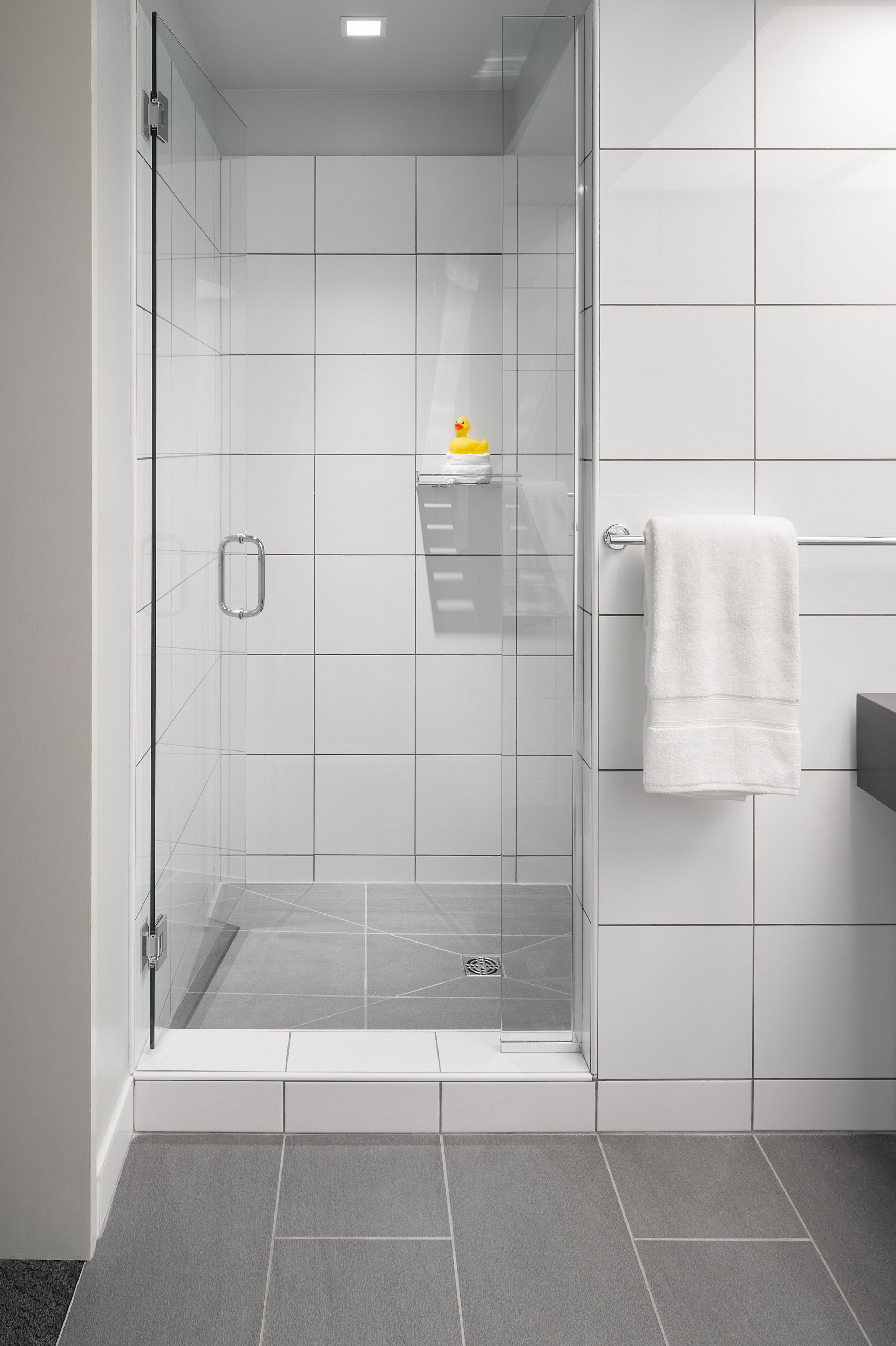 A modern bathroom with a glass-enclosed shower, white tiles, and a towel rack.