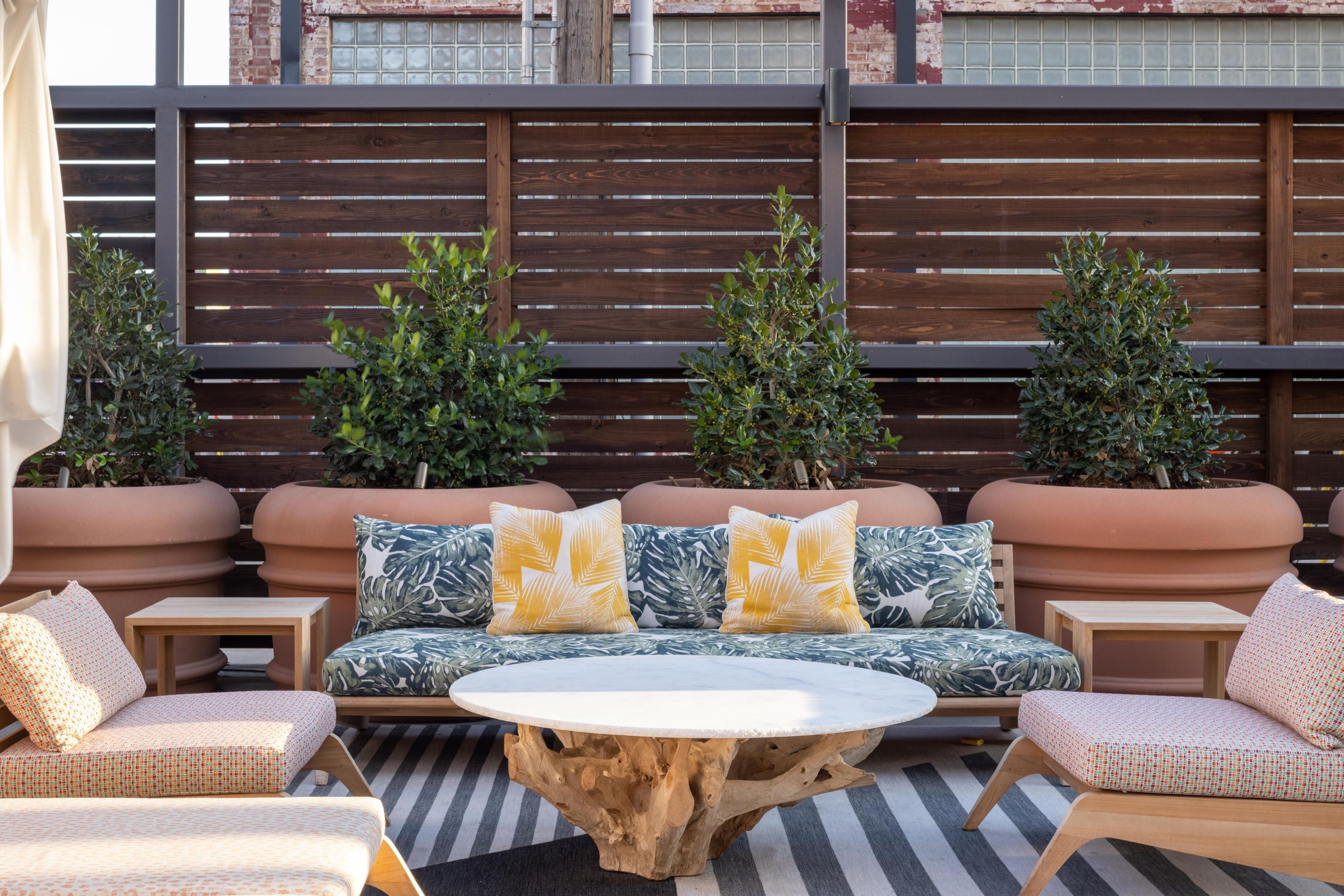 A cozy outdoor seating area with a round wooden table, cushioned sofas, and potted plants.