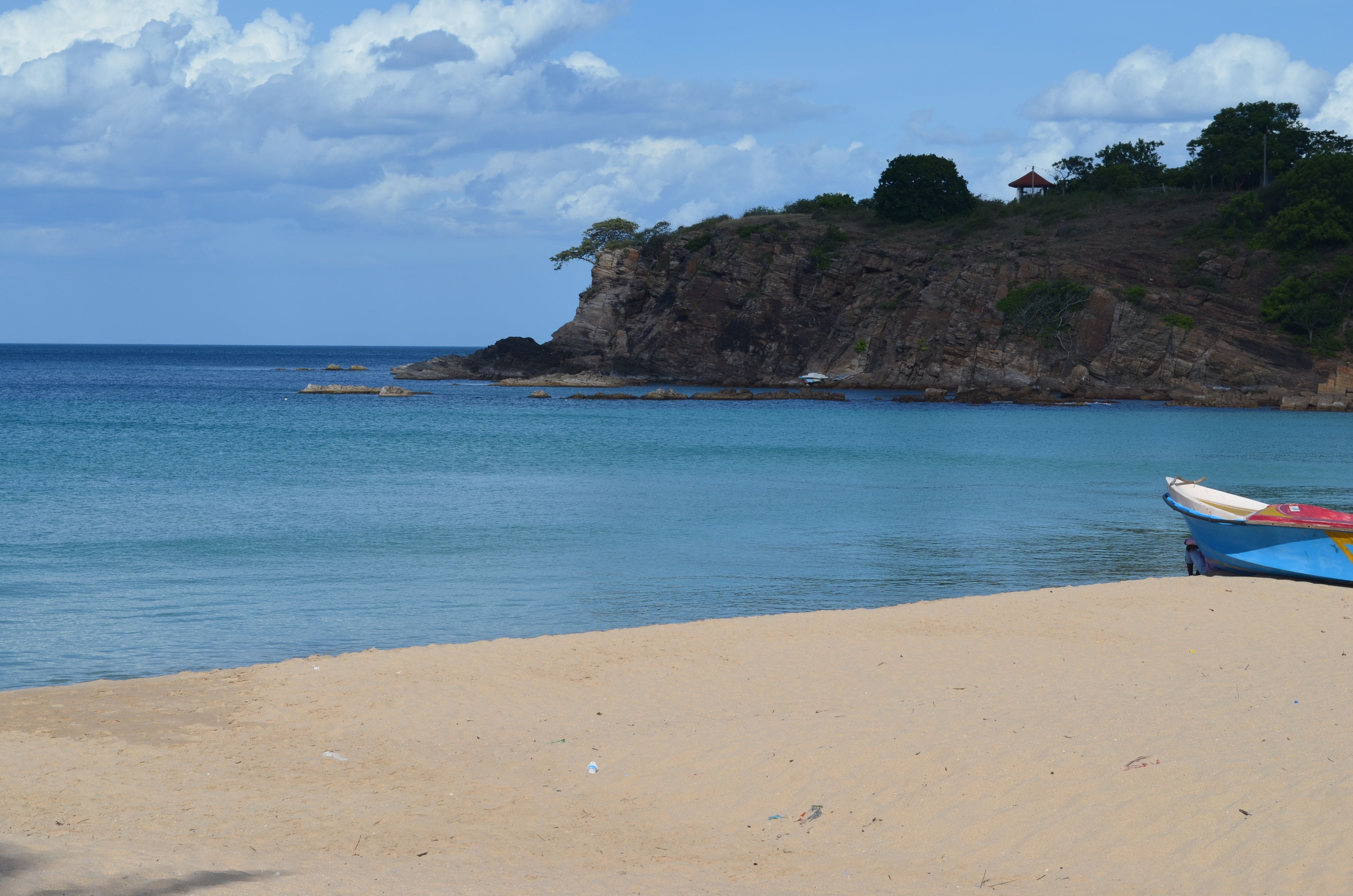 Uma praia com um barco na areia e um penhasco rochoso ao fundo.