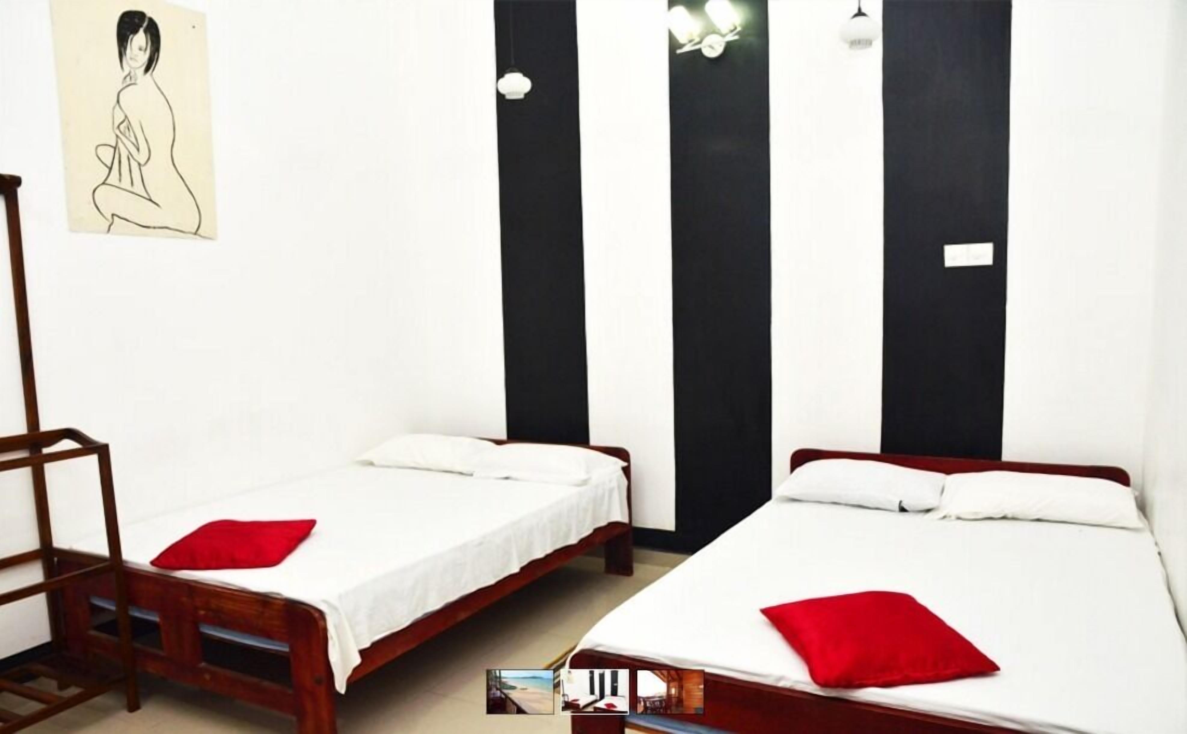 Habitación con dos camas individuales, cada una con una almohada roja y ropa de cama blanca. Se observa una escalera de madera y una silla en la esquina. Una pared a rayas negras y blancas se encuentra sobre las camas.