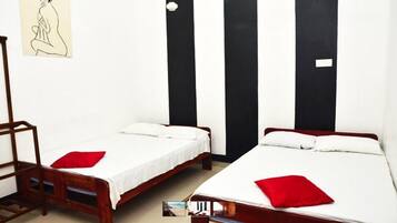 Habitación con dos camas individuales, cada una con una almohada roja y ropa de cama blanca. Se observa una escalera de madera y una silla en la esquina. Una pared a rayas negras y blancas se encuentra sobre las camas.