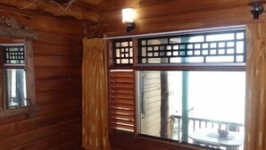A wooden cabin room with a large window, wooden walls, and a small table outside. - Dyke rest (Trincomalee)