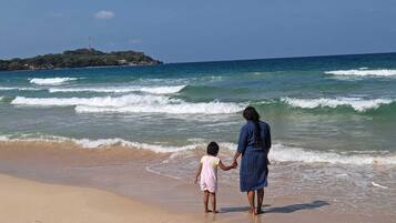 Escena de playa con una persona y un niño tomados de la mano, mirando hacia el océano.