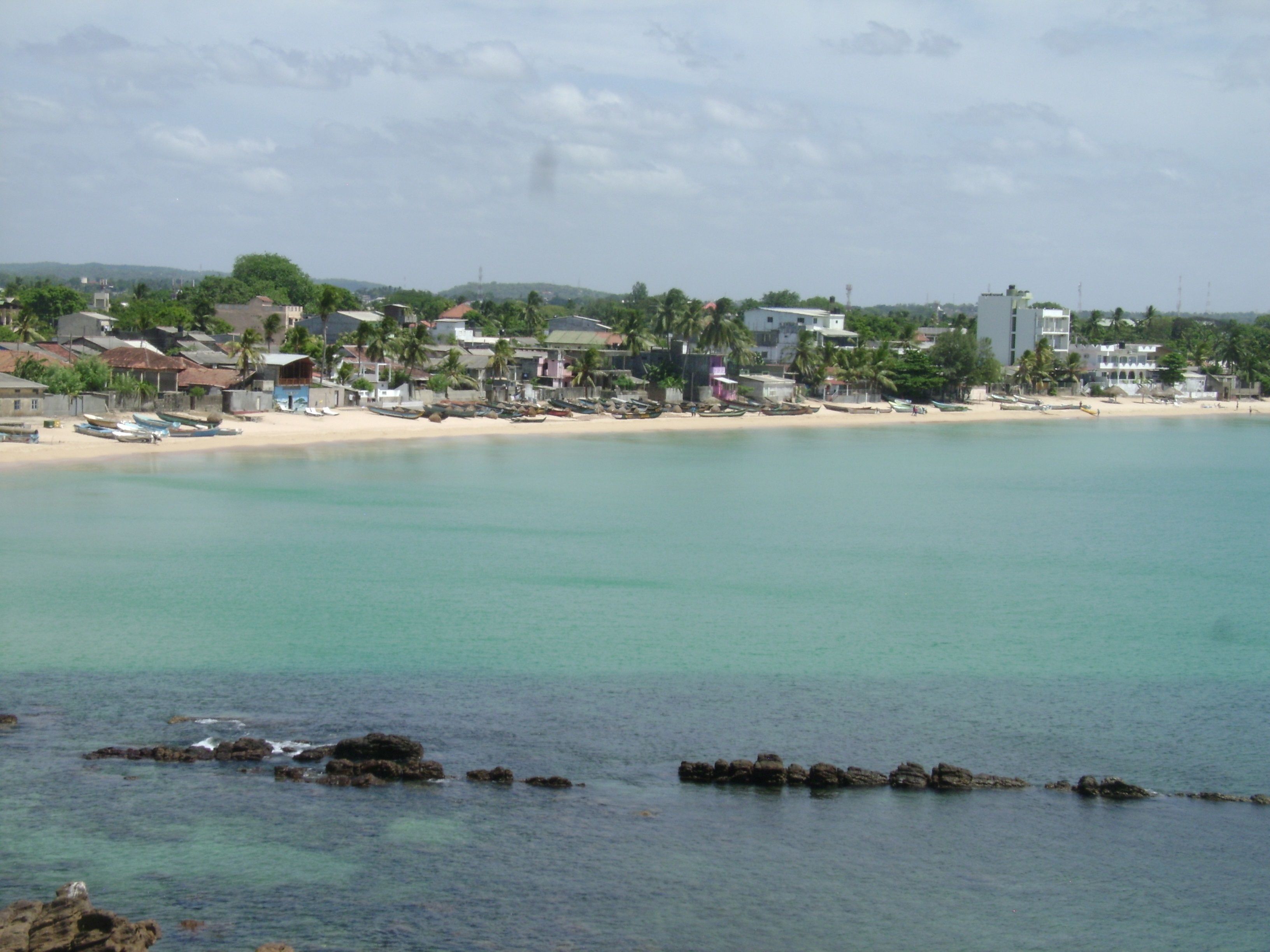 Eine Küstenstadt mit einem Sandstrand, klarem türkisblauem Wasser und Gebäuden entlang der Küste.