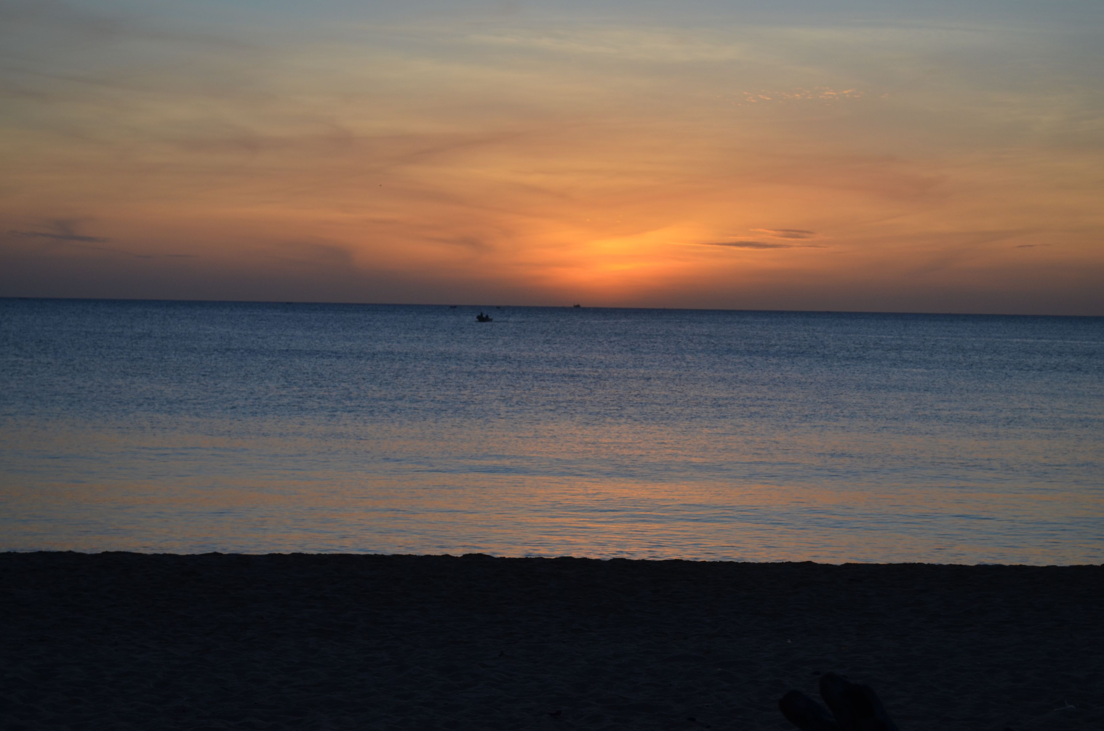 A beach at sunset with calm waters and a distant boat.