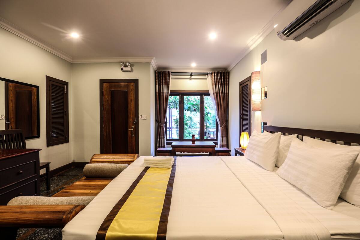 A hotel room with a large bed, a desk, and a view of greenery outside.