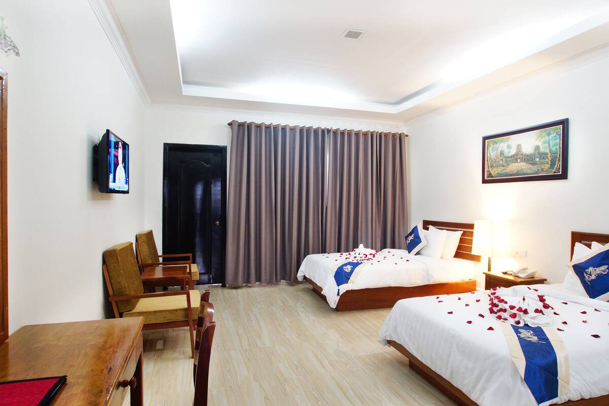 Une chambre d’hôtel avec deux lits, un bureau, une chaise, une télévision et un tableau au mur.