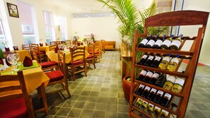 A restaurant interior with wooden chairs and tables, a wine rack with various bottles, and a large potted plant. - Dinata Angkor Boutique Hotel (Siem Reap)