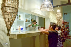 A bar area with a counter, shelves with bottles, and hanging lights. - Dinata Angkor Boutique Hotel (Siem Reap)