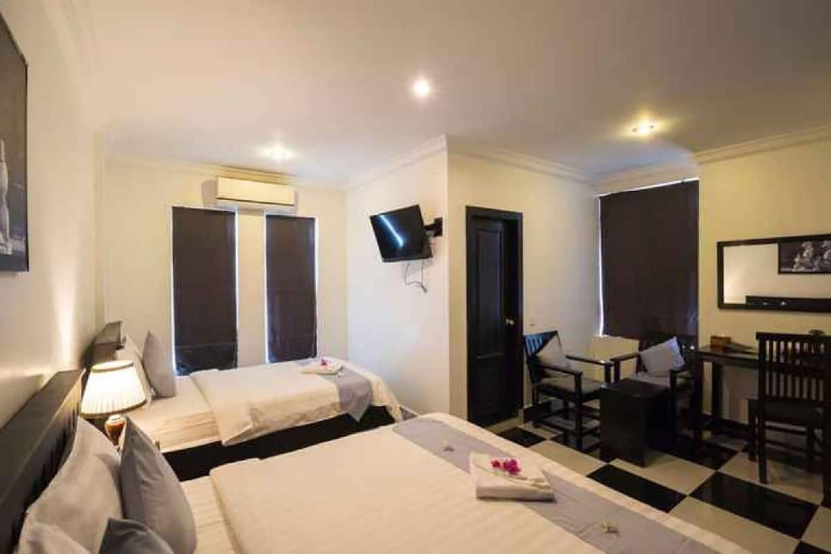 A hotel room with two beds, a desk, a chair, a TV, and a door.
