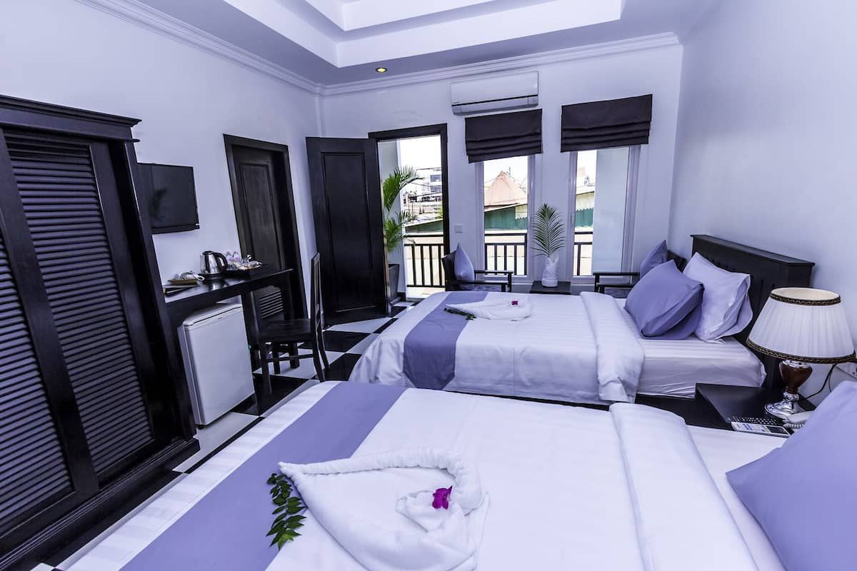 A hotel room with two beds, a desk, and a view of the outside.