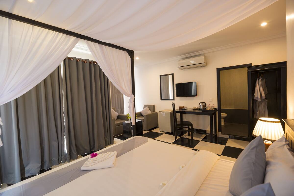 A hotel room with a bed, a desk, a chair, a television, and an air conditioning unit.