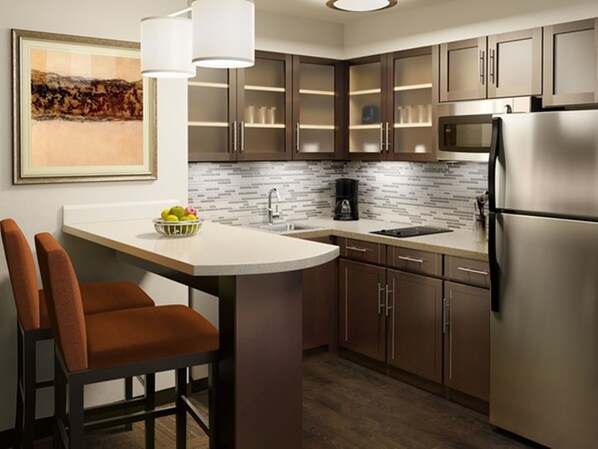 A modern kitchen with dark wooden cabinets, a white countertop, and a stainless steel refrigerator. - Staybridge Suites Miamisburg by IHG (Miamisburg)