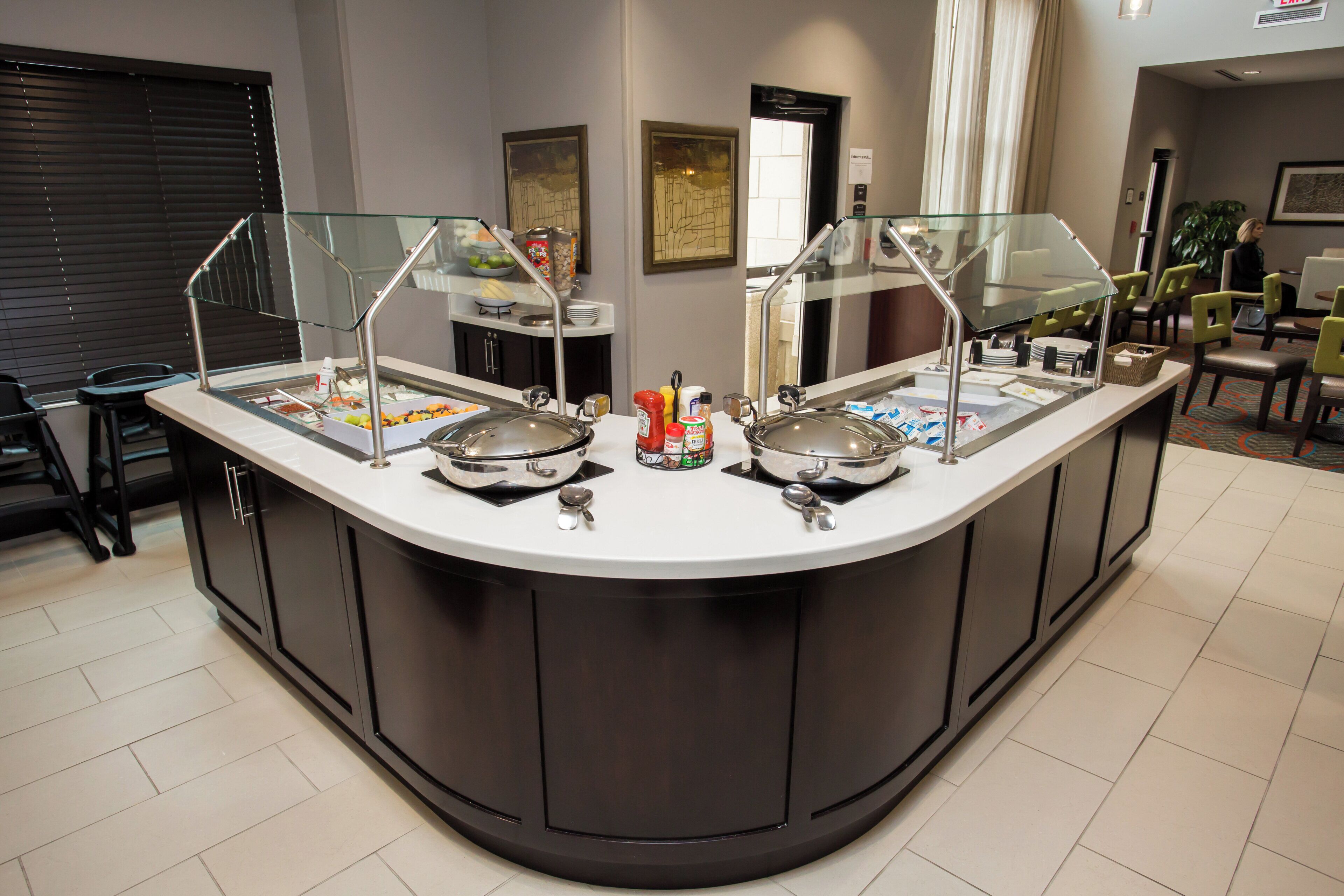 A buffet counter with multiple food stations, a glass enclosure, and a variety of condiments.