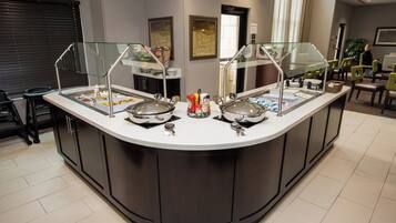 A buffet counter with multiple food stations, a glass enclosure, and a variety of condiments.