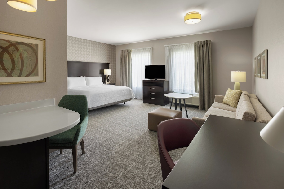 A hotel room with a bed, a desk, a chair, a sofa, a television, and a small table.