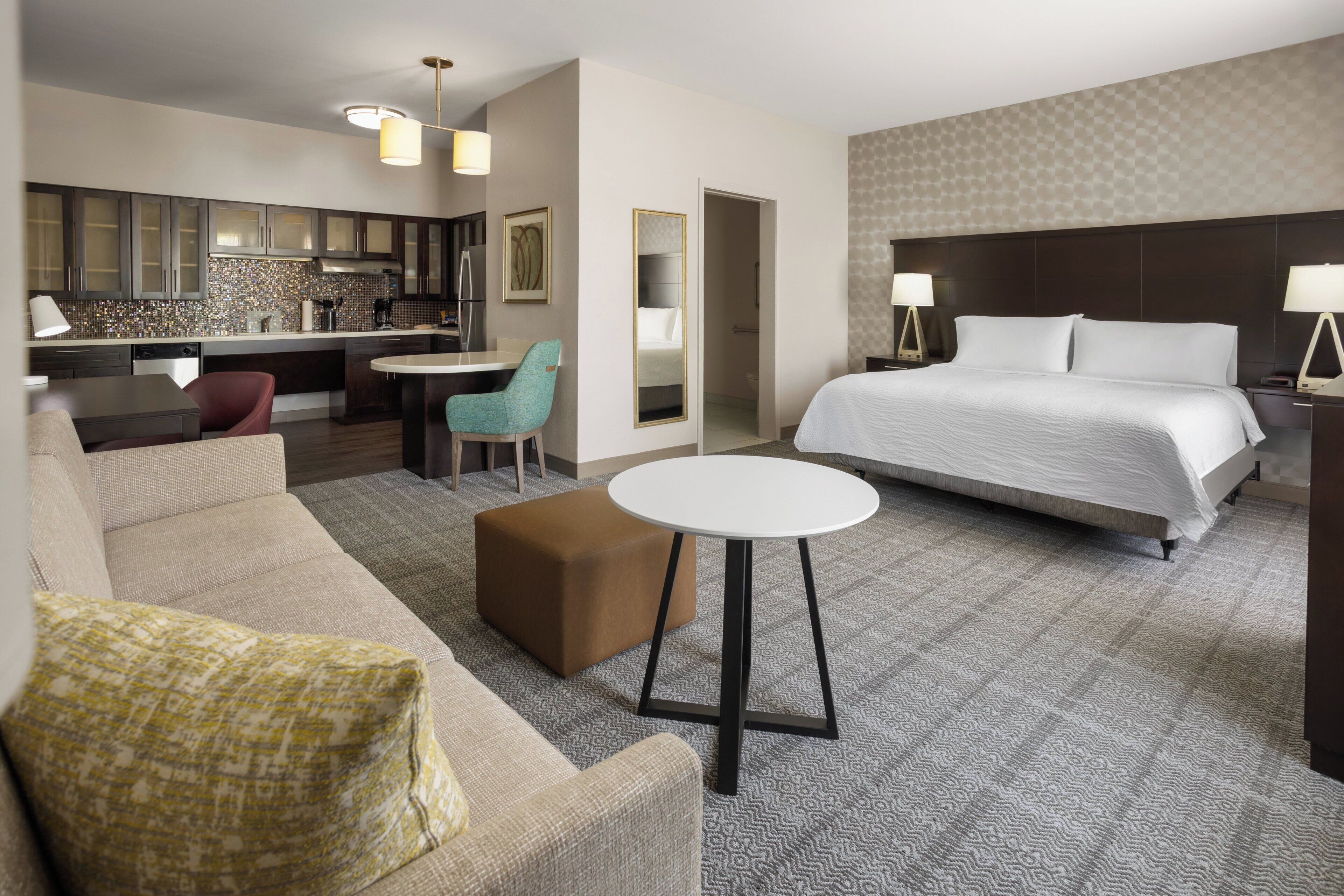 A hotel room with a bed, a sofa, a small table, a kitchenette, and a bathroom.